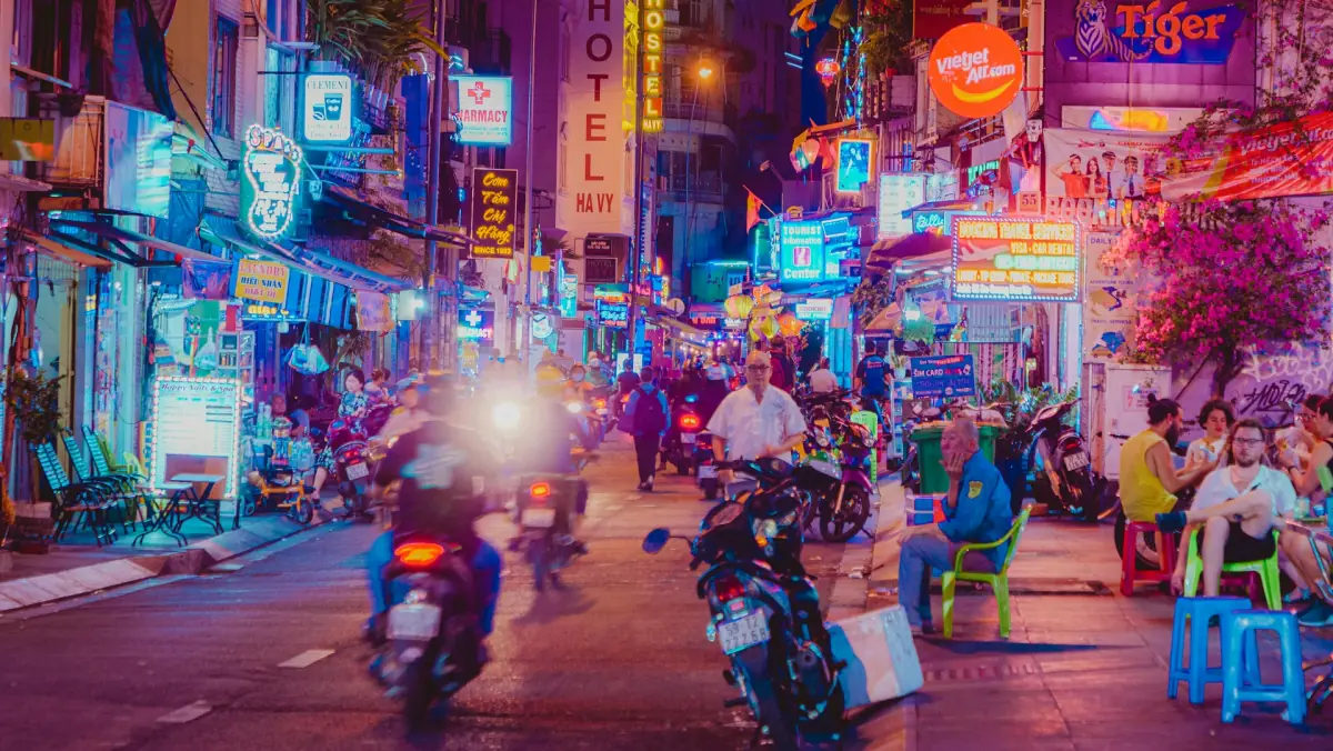 Neon-lit street at night with people and motorbikes