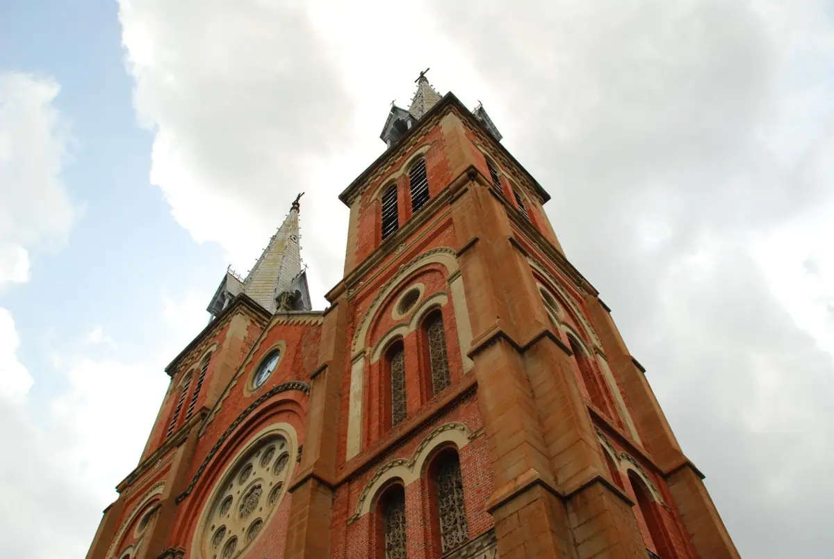 Red brick towers of Notre-Dame Cathedral against a cloudy sky