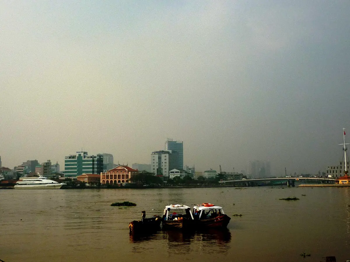 Boote auf dem dunstigen Saigon-Fluss mit niedrigen Gebäuden am Ufer