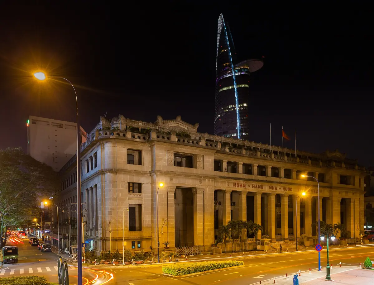Neoklassizistisches Bankgebäude bei Nacht beleuchtet, dahinter der Bitexco Tower